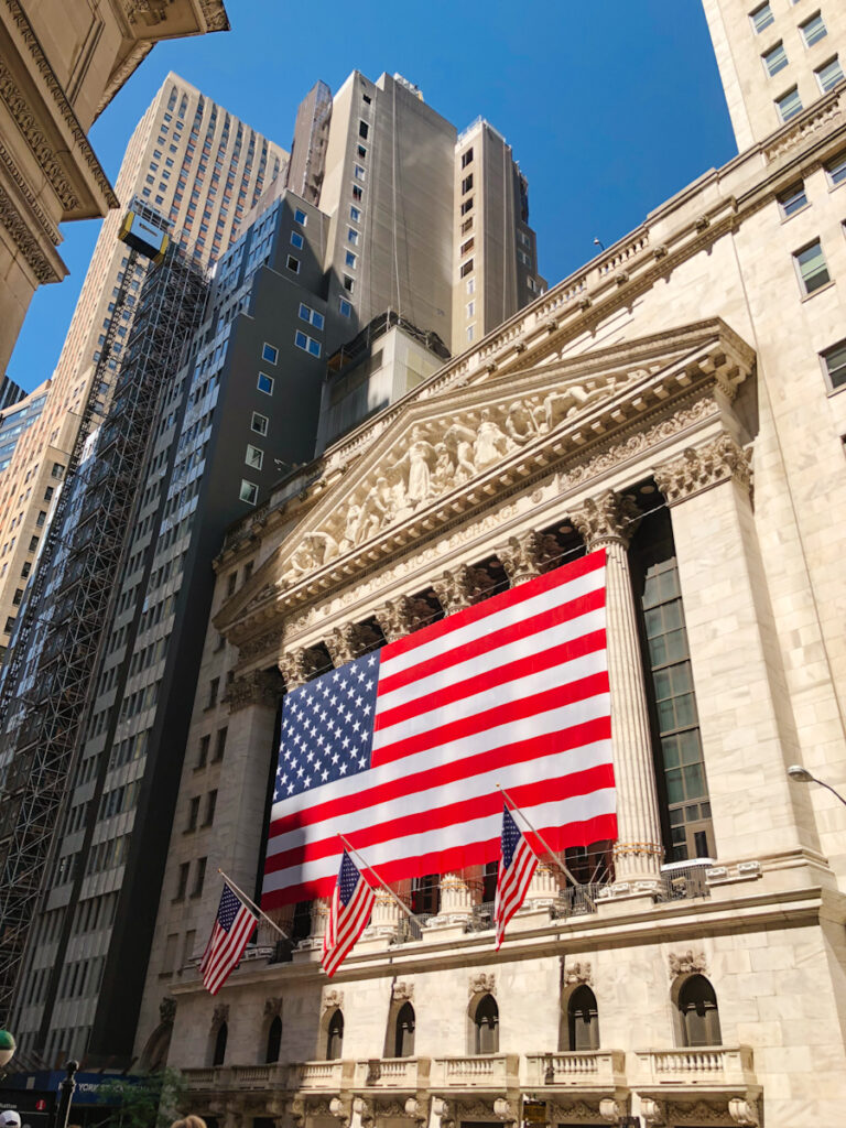 Exterior of New York Stock Exchange building with American flag on the outside of a massive pillar facade