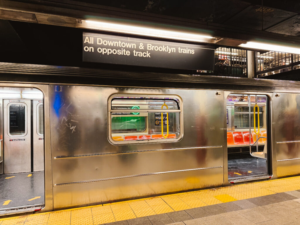 Explore New York City by using the extensive subway system, where a subway car is shown here with a sign above that reads "All Downtown and Brooklyn lines on opposite track"