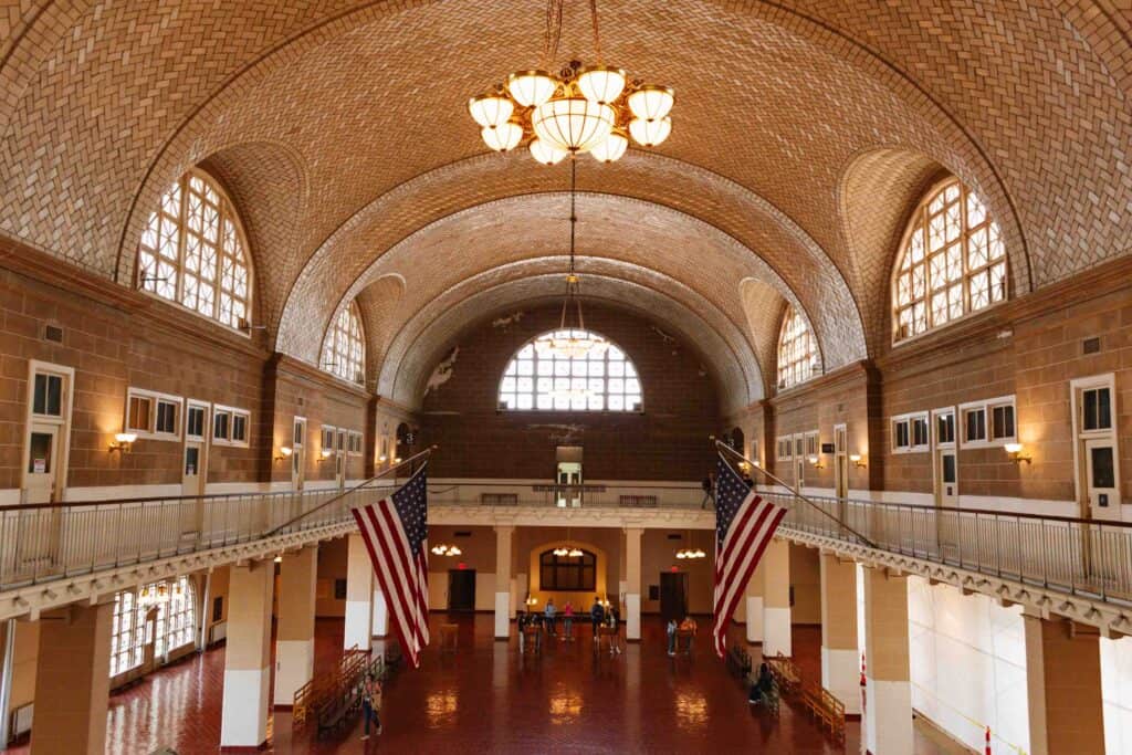 Ellis Island Museum of Immigration processing center room with large arched ceiling, American flags on the sides, and brown tiled floor