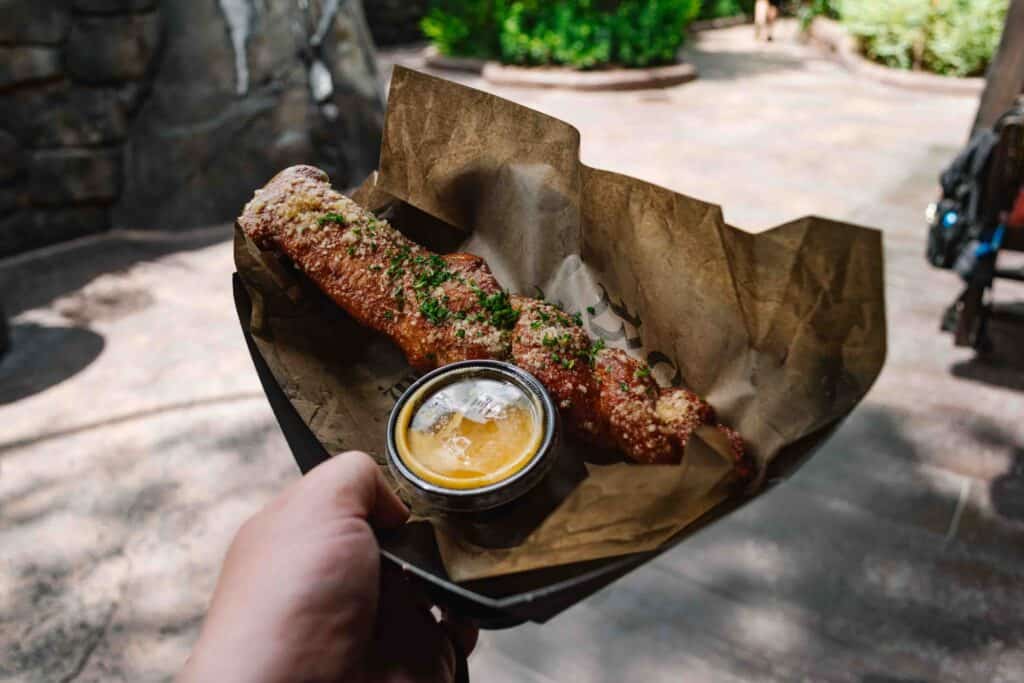 Woman's outstretching hand hold a garlic pretzel with a butter dipping sauce