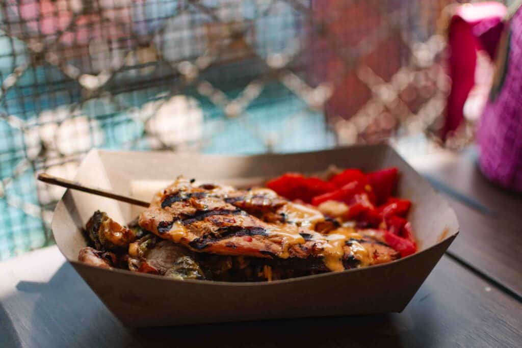 Grilled chicken on a skewer on top of farro, brussel sprouts, red bell peppers, and smoky cheddar sauce, one of the most healthy things to eat at Epic Universe