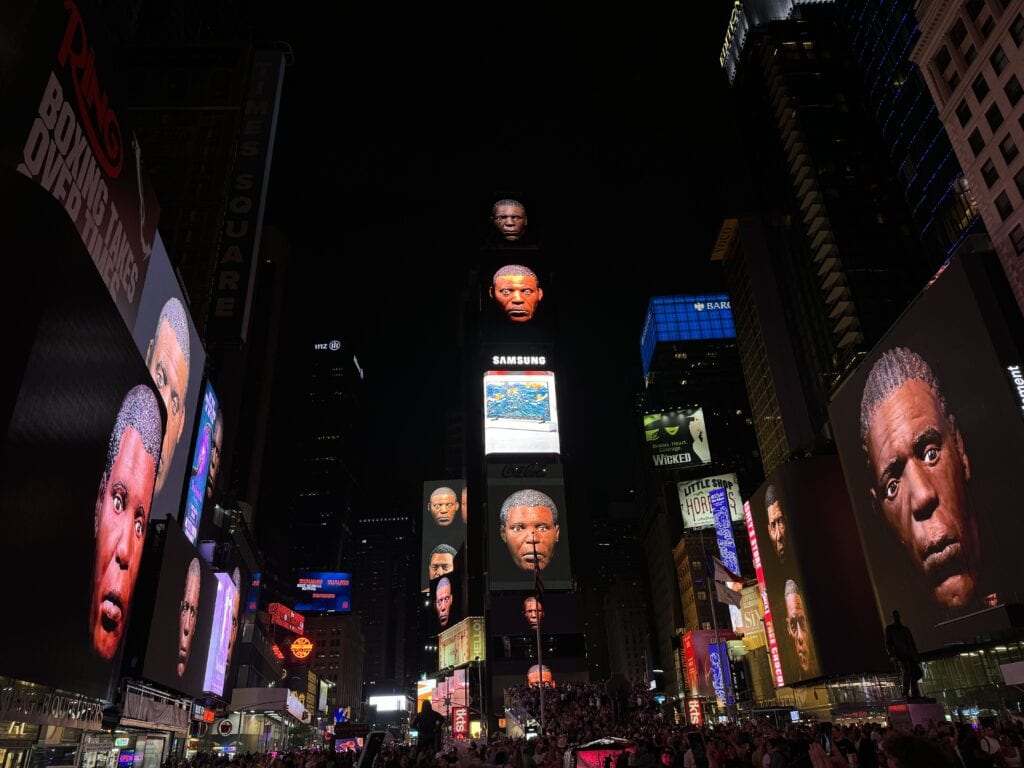 Times Square where the billboards ads are replaced with art, specifically digitally captured claymation of mens' heads