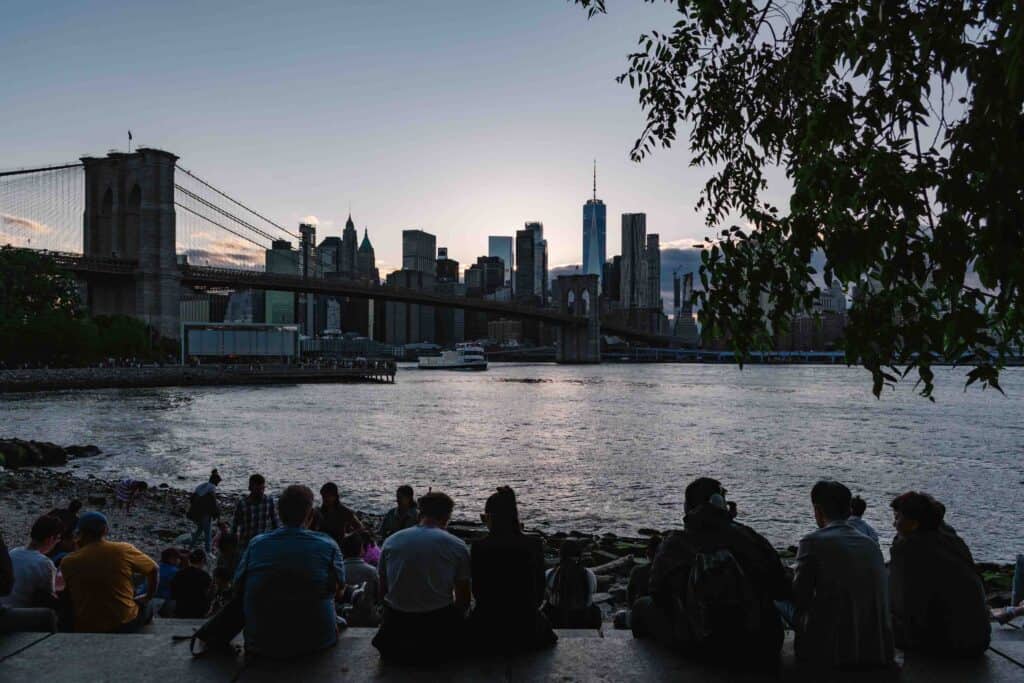People sitting on Pebble Beach in Brooklyn at blue hour looking at the Manhattan skyline