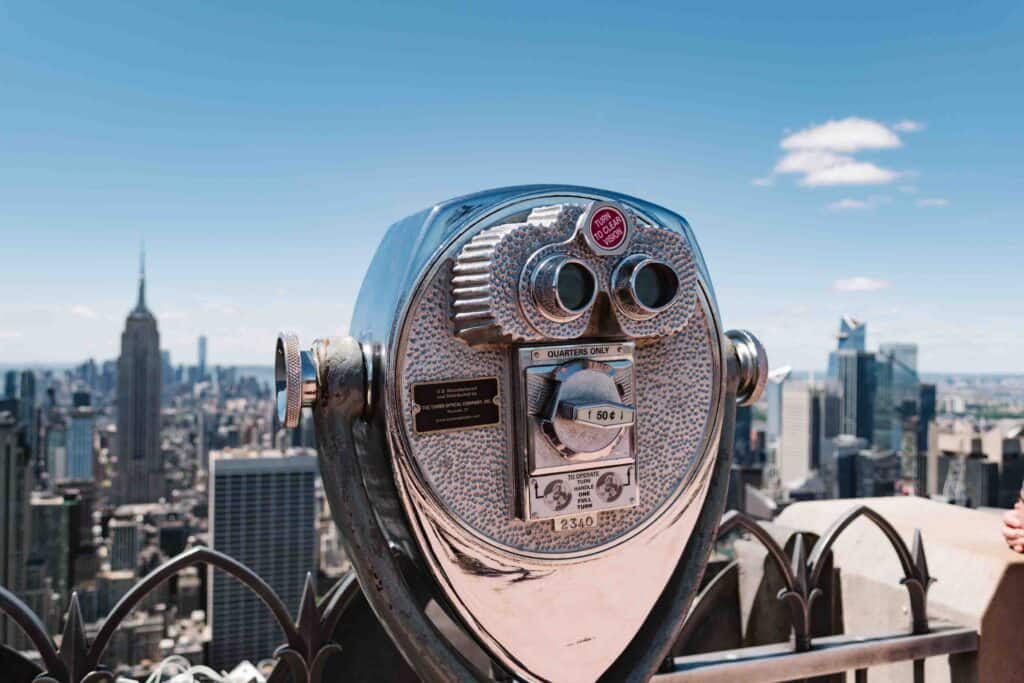 Old fashioned stationary binocular telescope on the top of Top of the Rock observation deck in New York with Empire State Building to the south in front