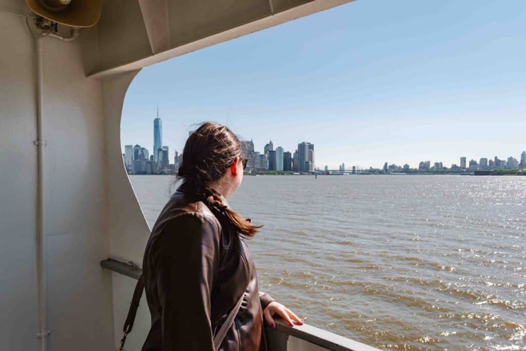 Woman looking past the side of a ferry toward the Manhattan ferry skyline in the morning