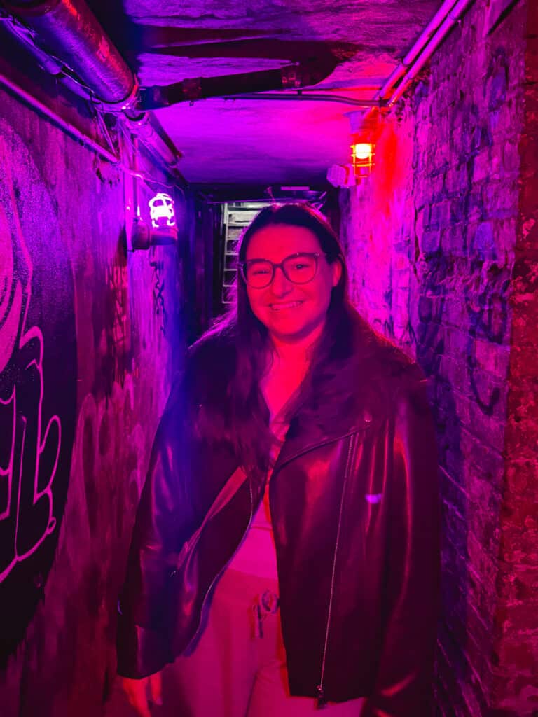 Woman posing in a graffiti covered tunnel that has purple and pink lights