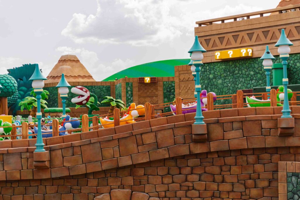 Super Nintendo World's Yoshi Adventure ride view from the side (not on the ride) of the multicolored yoshi ride cars traveling through the world