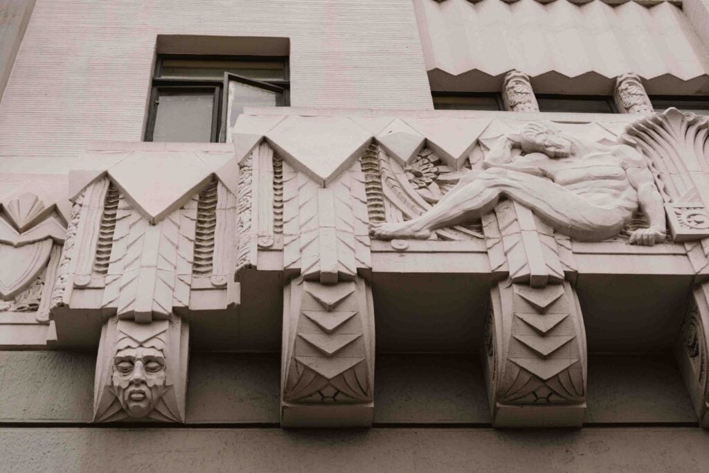 Exterior of apartment building in Long Beach, which is grey and has big blocked art deco details like faces and men with chevron details
