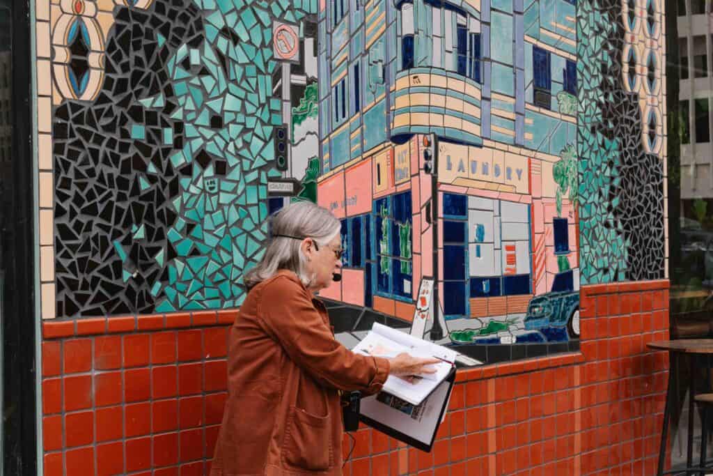 Long Beach Heritage architecture tour of the East Village Arts District downtown with an elderly woman pointing to a printed image in front of a massive tiled wall
