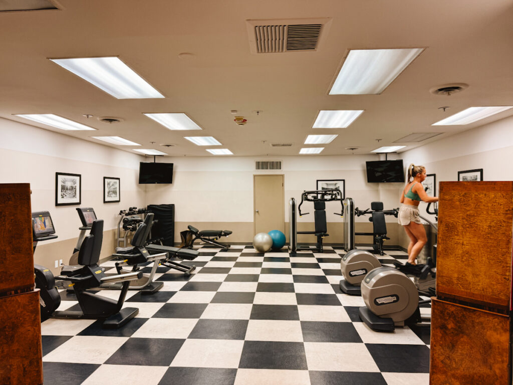 Inside The Queen Mary's fitness center with black and white checkered floor, cardio machines to the right and weight equipment to the left.