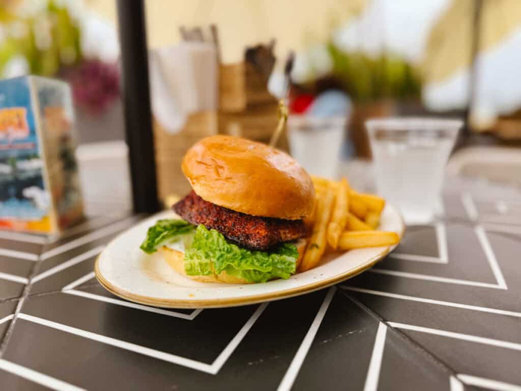 Blackened salmon burger with lettuce and held together with a toothpick and with a side of fries on an outdoor beachside restaurant table