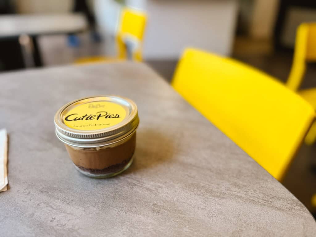 Small pie in a jar with a yellow label that reads Cutie Pie, on a marble table with yellow chairs