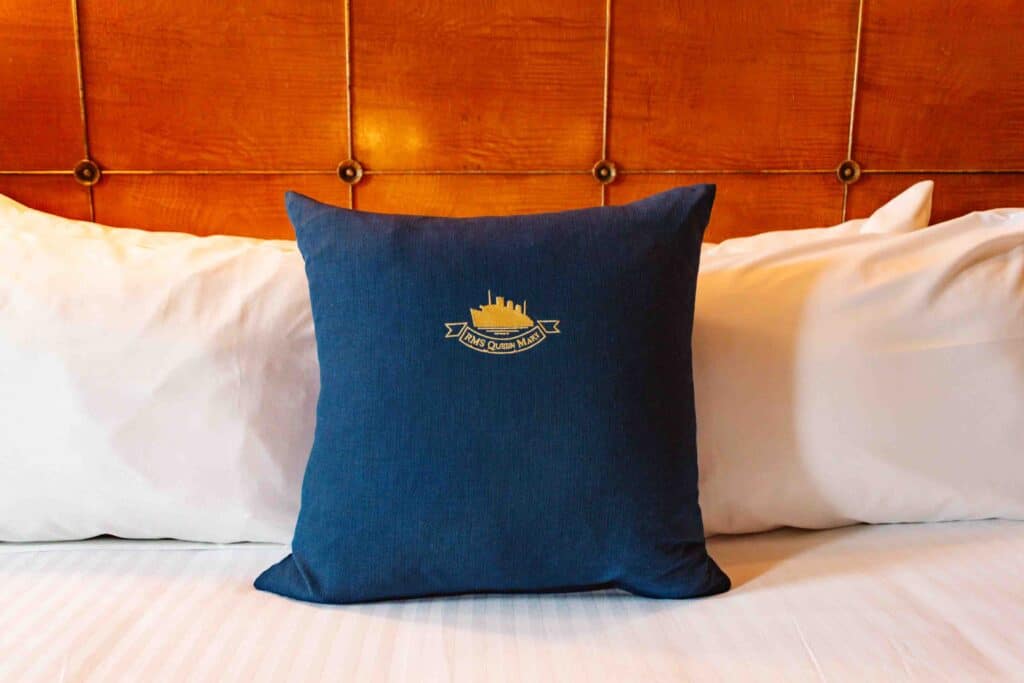 RMS Queen Mary embroidered blue pillow on a bed of modern white bedding