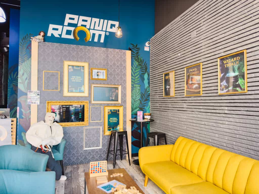 Inside of PanIQ Escape Rooms in Long Beach with a yellow couch to the right and blue one to the left, with a mannequin in a straight jacket sitting in a chair