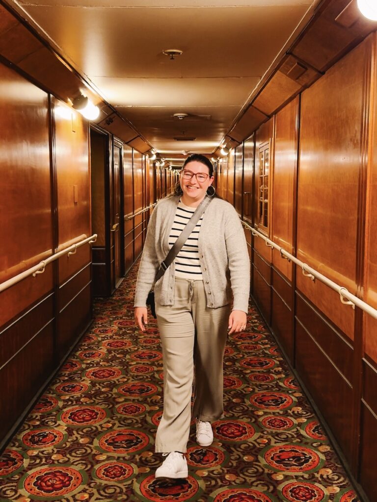 Woman walking and smiling down a hotel hallway designed in the 1930s.