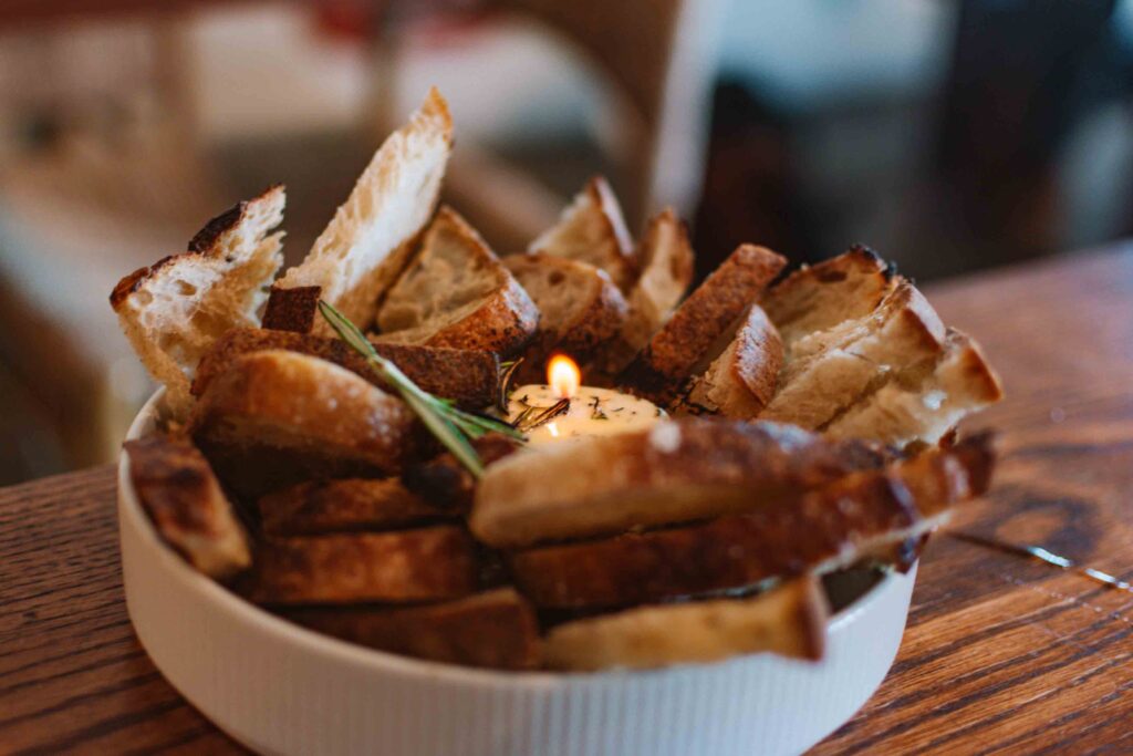 Round flat bowl filled with slices of sourdough bread with an herb butter candle lit in the center with a sprig of rosemary on top