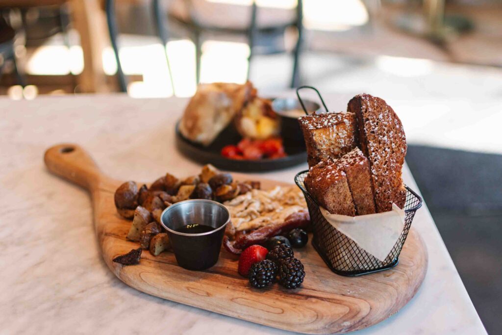 Charcuterie board of breakfast items like french toast sticks, berries, eggs, bacon, and potatoes