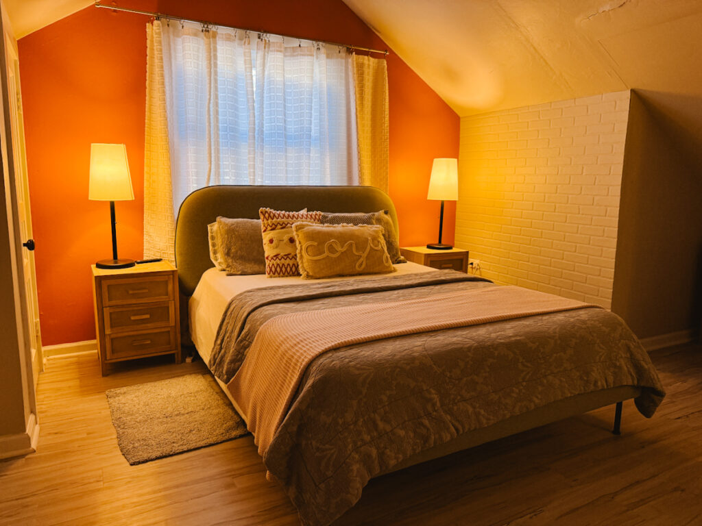 Interior of a loft BnB space showing the bedroom under an arched ceiling and bed that has a pillow that reads Cozy