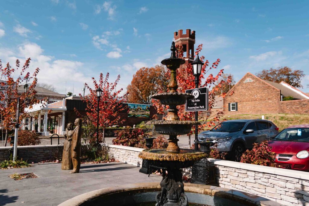 Angled view from the corner of a small park which has a fountain, two statues of our 11th president and his wife, with an historic tower in the background and a Maury County mural on a building behind