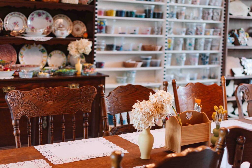 View a beautiful wood dining table with a wall of craft materials behind in a craft cafe.