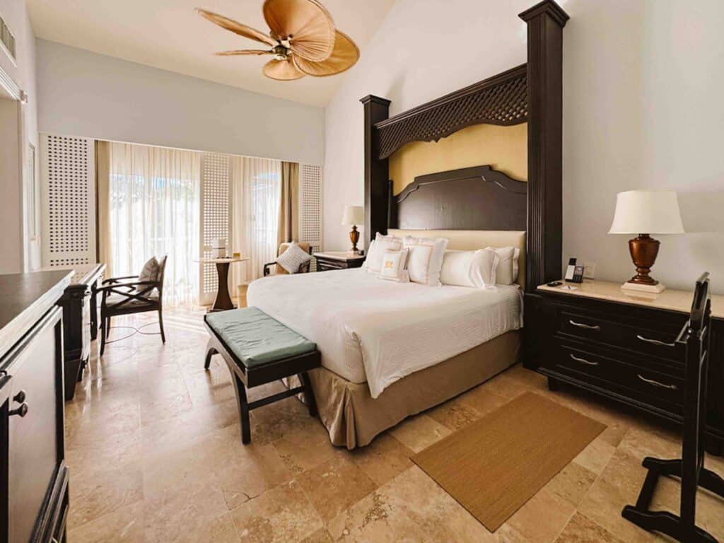King room at an all inclusive in Mexico called Royal Hideaway Playacar with high ceilings, a desk and chair, TV, fridge, and large nightstands