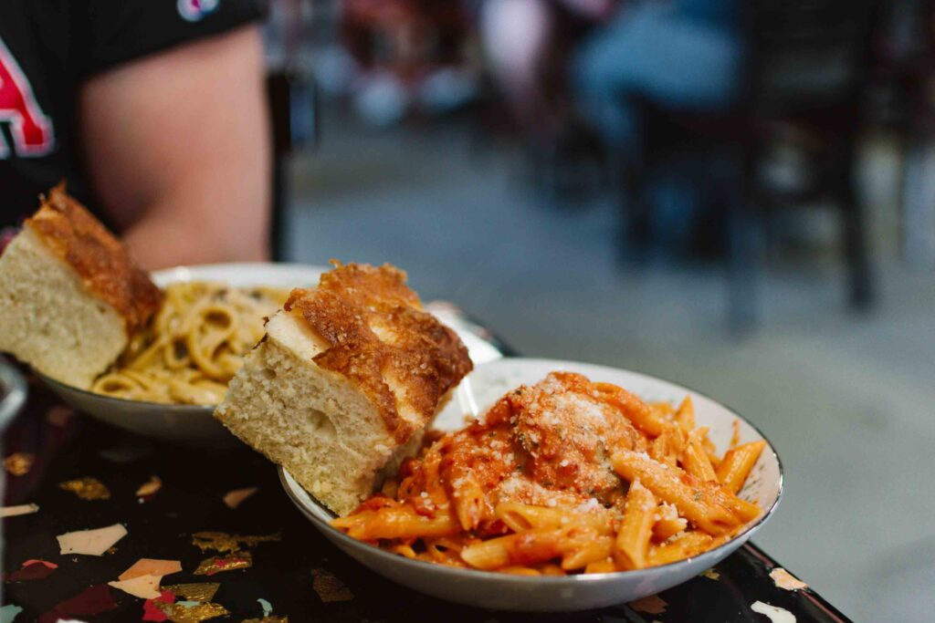 Two plates of pasta - one red sauce, one white - both with a swuare of focaccia bread on top the left