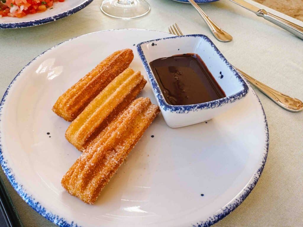 Churros with chocolate on the side on a white plate at a restaurant in Mexico