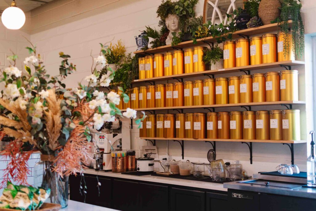 Tea shop counter where there's a bouquet to the left and a wall of gold tea canisters behind