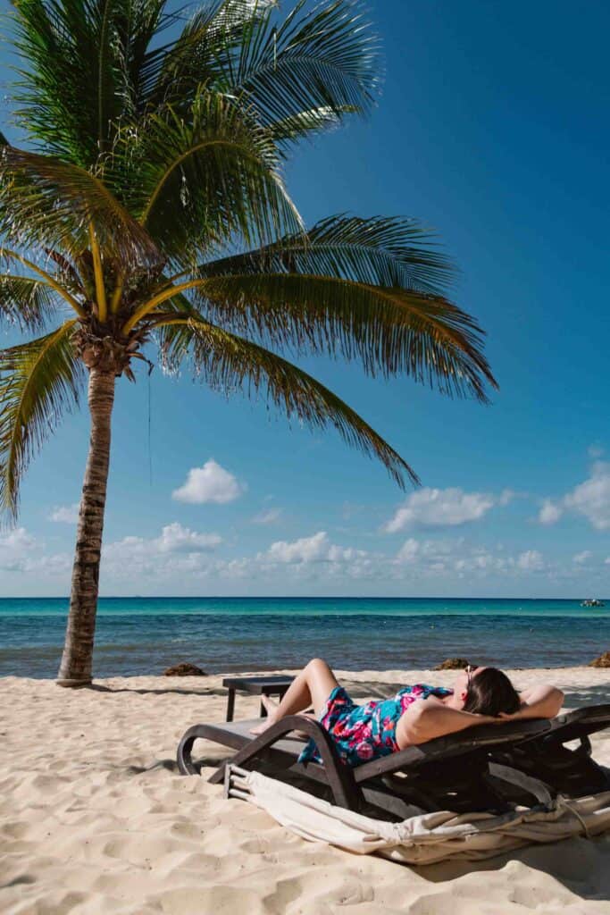 Woman laying back in a beach lounge chair relaxing at the beach with a palm tree to her left side, front