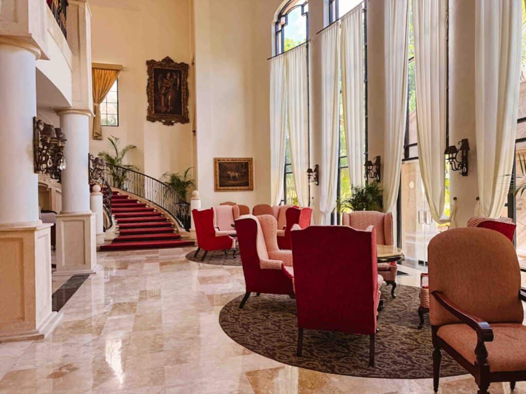 First floor of a lobby building with high backed red plush chairs and a staircase to the back of the room