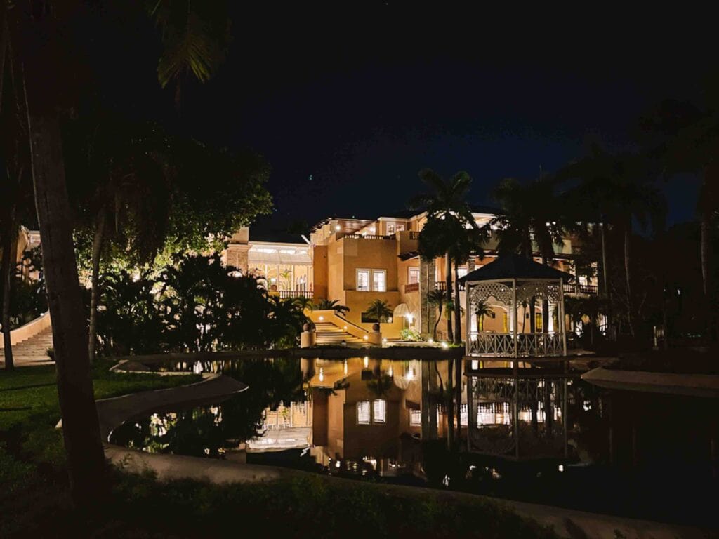 Night view of Royal Hideaway main building with lake and gazebo in front reflecting the lights of the building.
