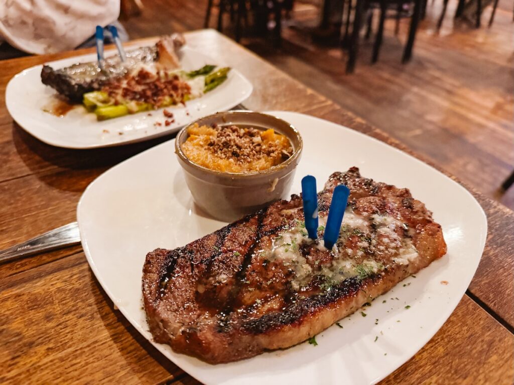 Plated NY strip steak seasoned with butter on top and a small cup of mashed sweet potatoes to the side