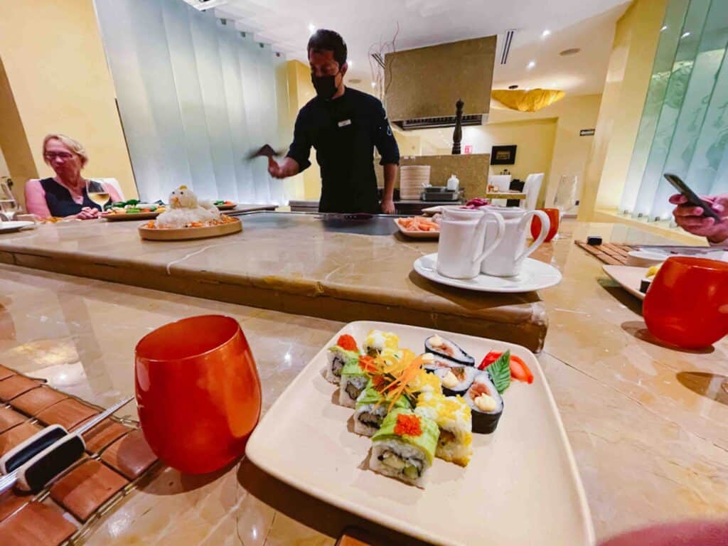 Chef cooking on an open grill at a teppanyaki restaurant where there is a plate of sushi in front of the person who took the photo