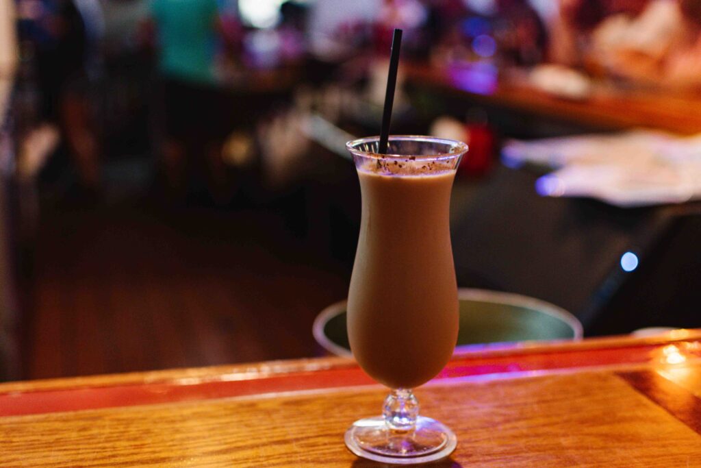 My favorite bushwhacker from Beach Kitchen and Cocktails where the drink is in a curvy pina colada type glass on a bar with high bokeh in the background