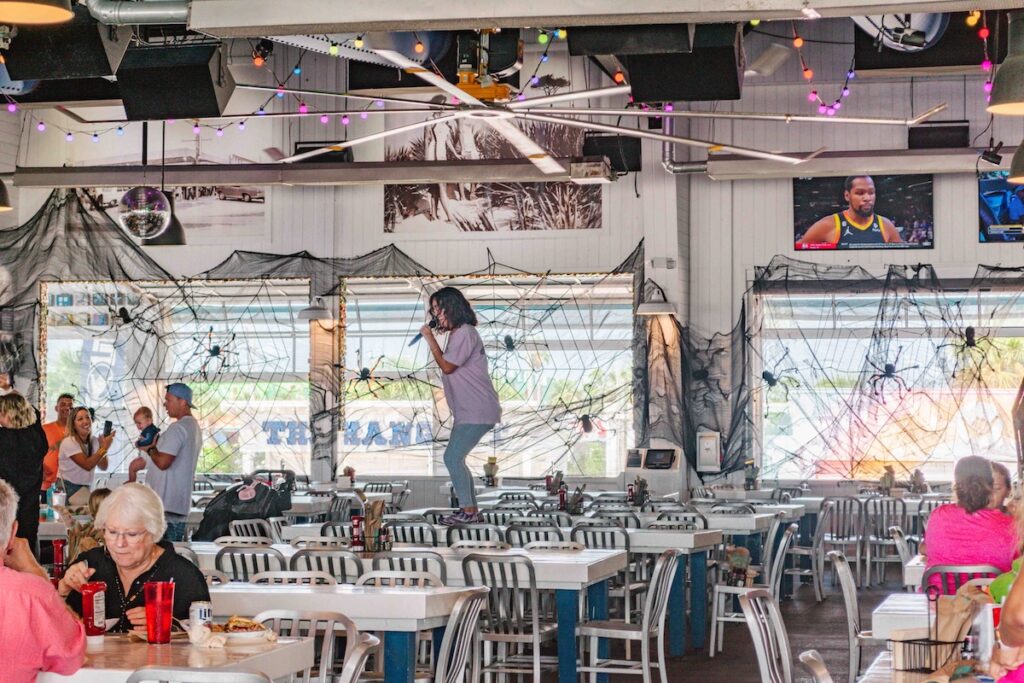 Waitress standing on a table singing and dancing with patrons of The Hangout, beachside restaurant