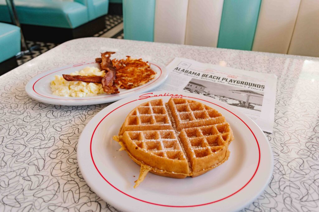 Sunliner diner breakfast of a waffle and side of egg whites and bacon with a newspaper menu on the booth table