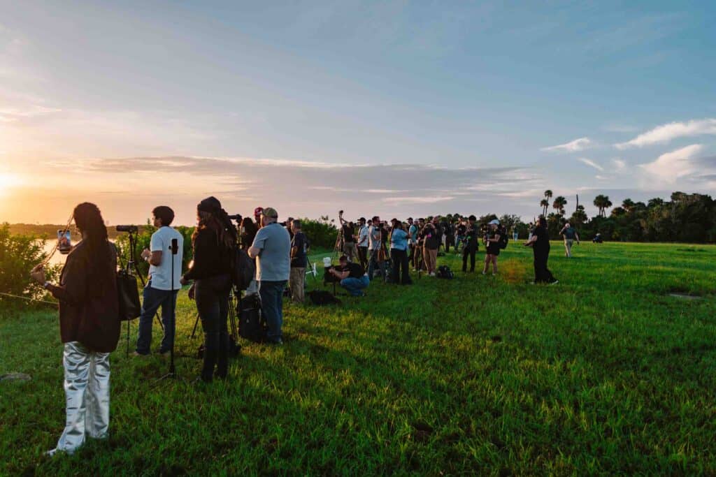 Early morning rocket launch at Kennedy Space Center with a crowd of people on the lawn waiting.
